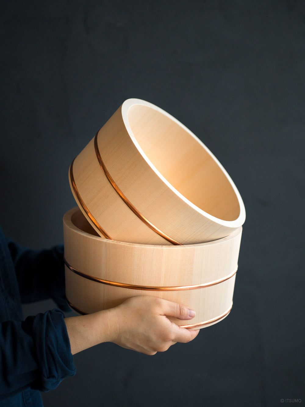Hands holding two Azmaya hinoki wood bath bowls with copper trim