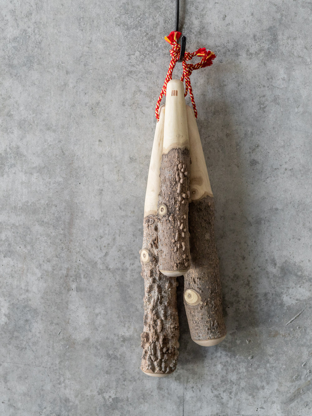 Group of Azmaya sansho wood pestles hanging from red string on a hook