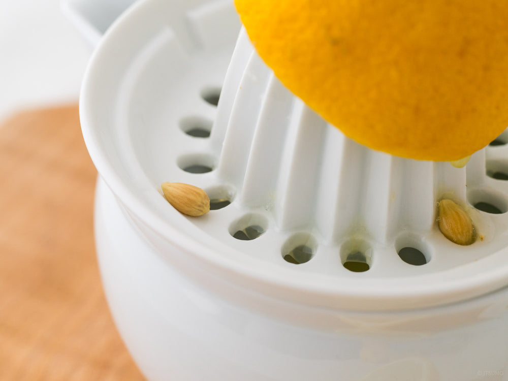 Azmaya white porcelain citrus juicer squeezing lemons with the seeds being caught in the top lid holes