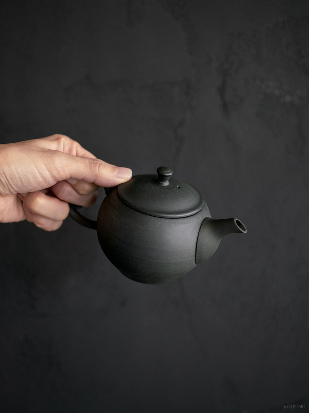 Handing holding matte black ceramic teapot made in Japan