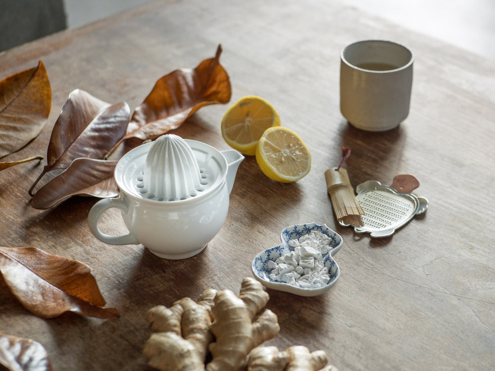 Azmaya white porcelain citrus juicer surrounded by lemons, tea, ginger and fall leaves