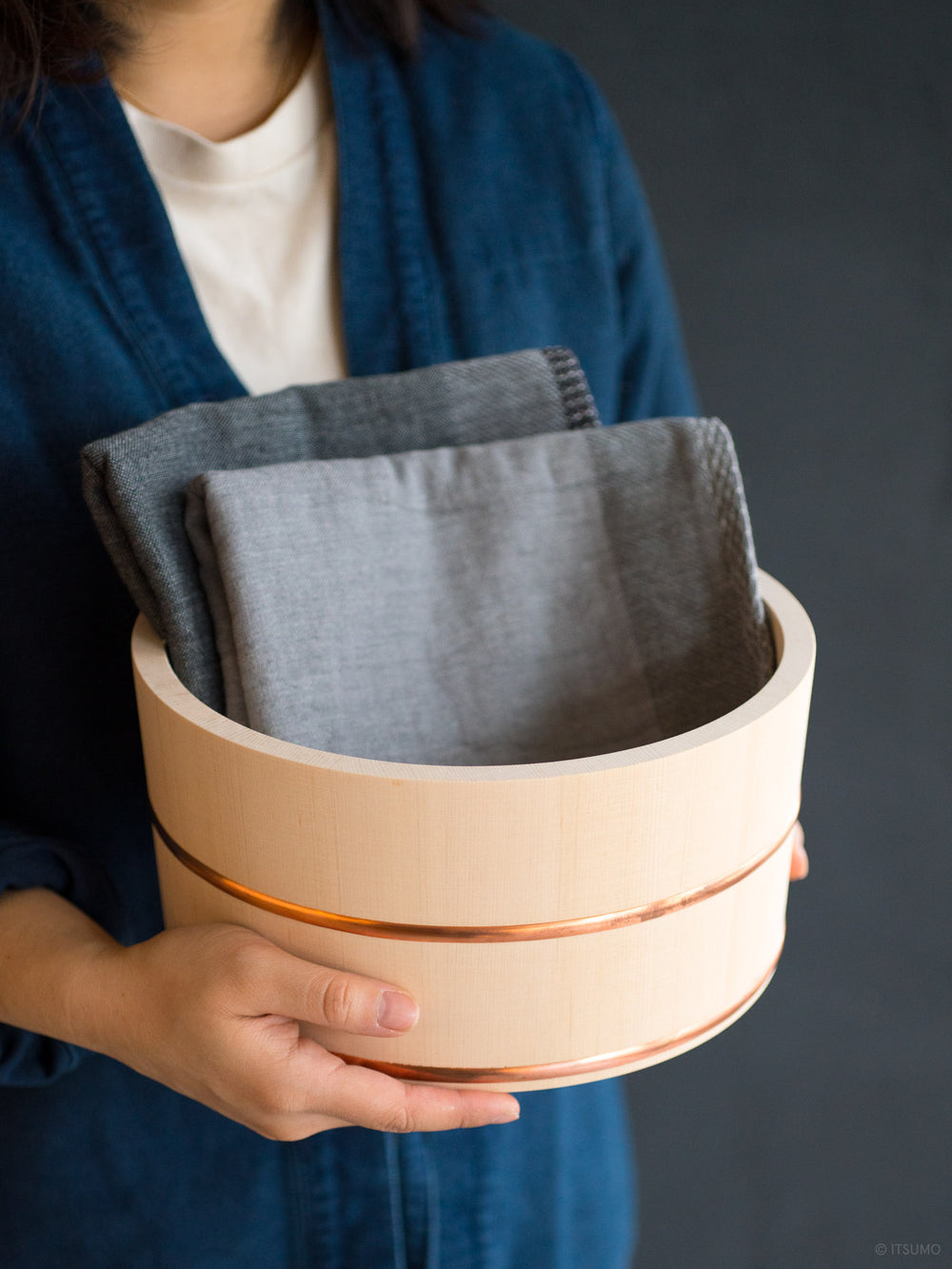 Hands holding an Azmaya hinoki wood bath bowl with towels inside
