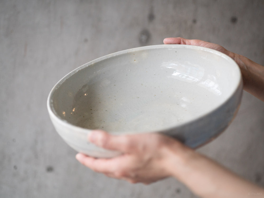 Hands holding a large ceramic serving bowl in a white sekkai glaze, handmade in Japan