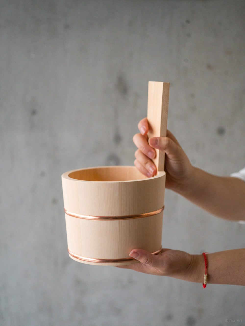 Hands holding a hinoki wood bath bucket with a handle and copper trim