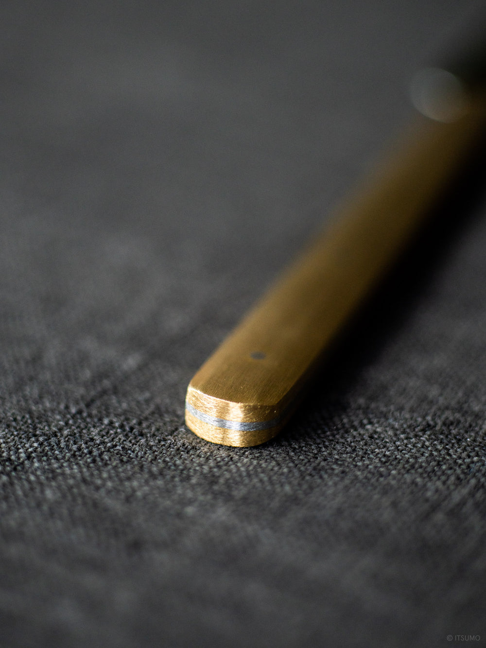 Close up of the brass handle of a stainless steel butter knife