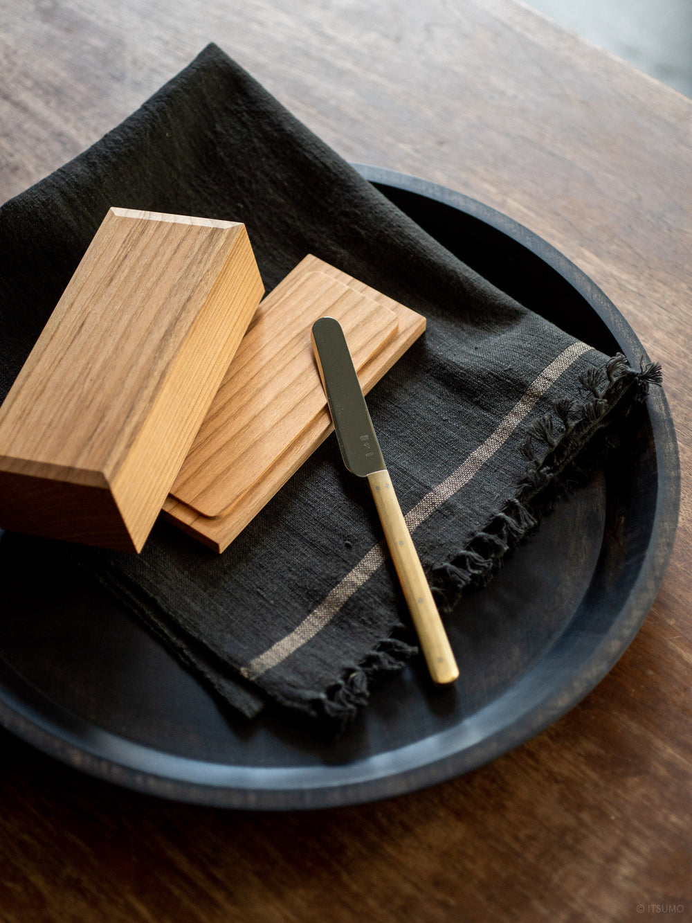 Azmaya cherry wood butter case next to a stainless steel brass handle butter knife, on top of a linen cloth and serving tray