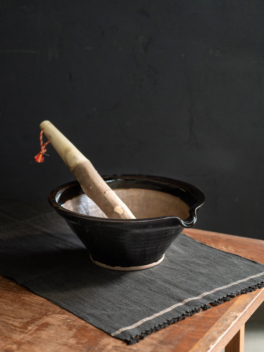 Azmaya's iga suribachi mortar in black glaze, with a wooden pestle leaning inside the bowl