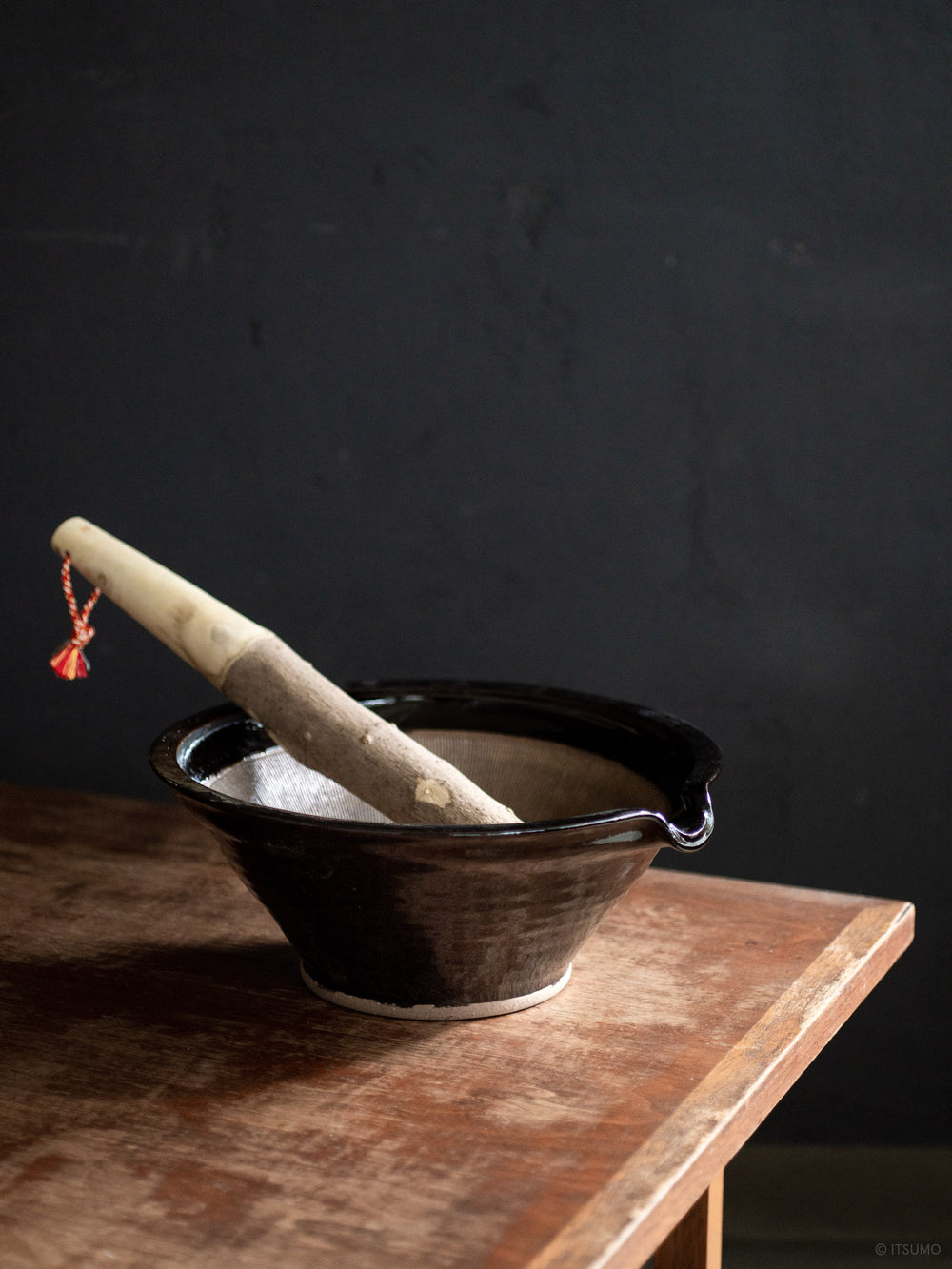 Azmaya's iga suribachi mortar in black glaze and a wooden pestle leaning inside the bowl