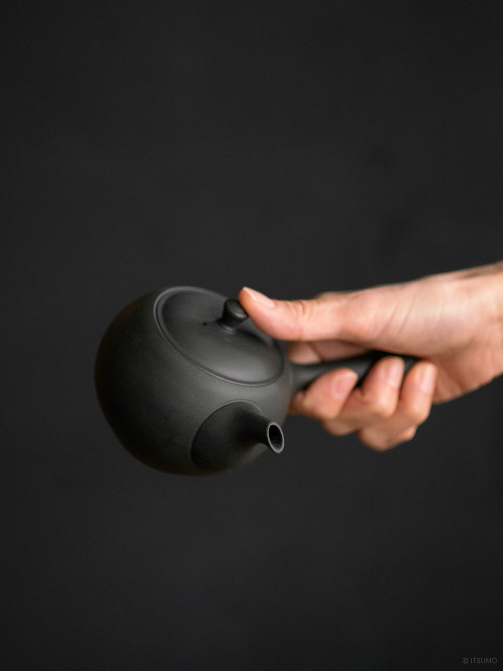 Hand holding the side handle on Azmaya's round teapot in unglazed matte black